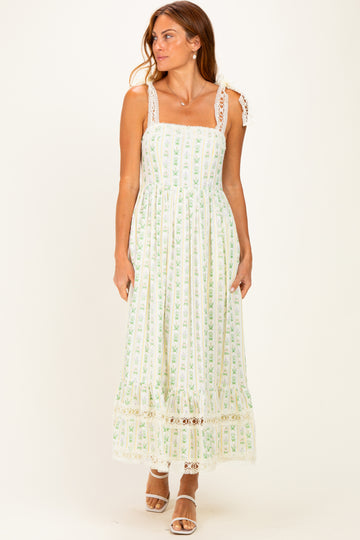 woman wearing a white and green floral maxi dress with lace trim and spaghetti straps