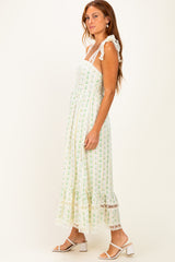 woman wearing a white maxi dress with green floral prints and lace details, styled with strappy sandals