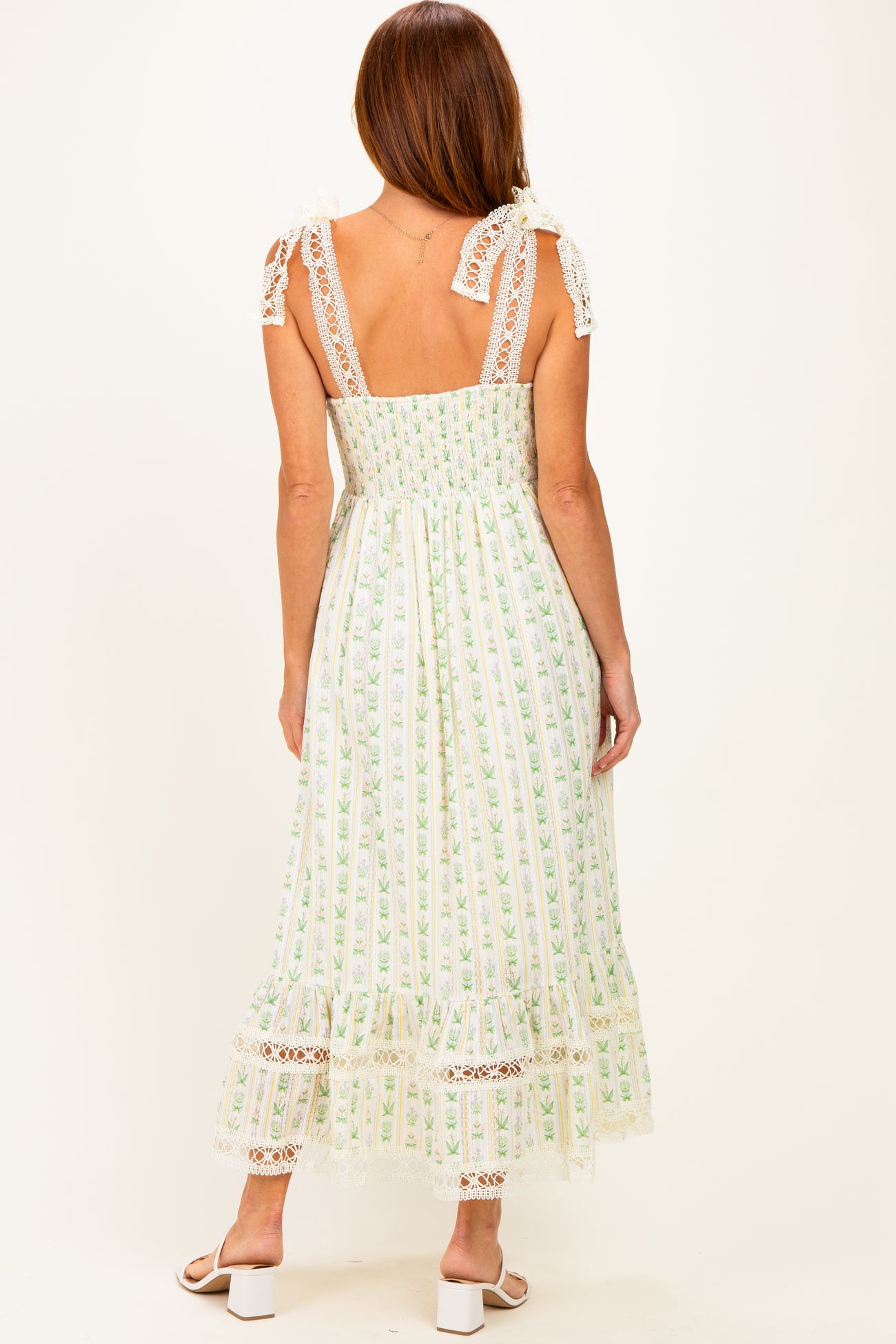 woman wearing a back view of a white floral maxi dress with lace details and adjustable straps