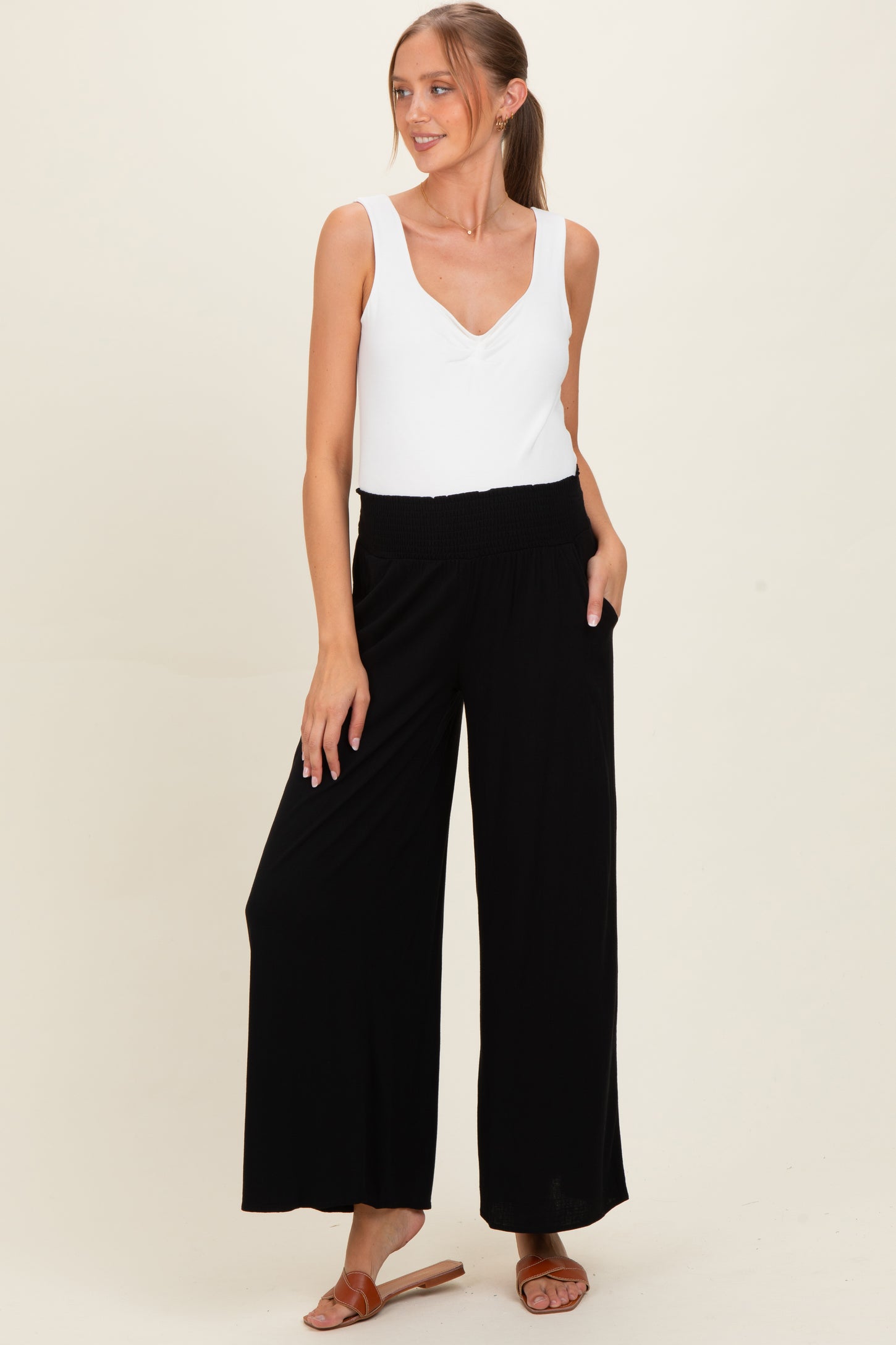 woman wearing a white sleeveless maternity top and black wide-leg maternity pants with pockets