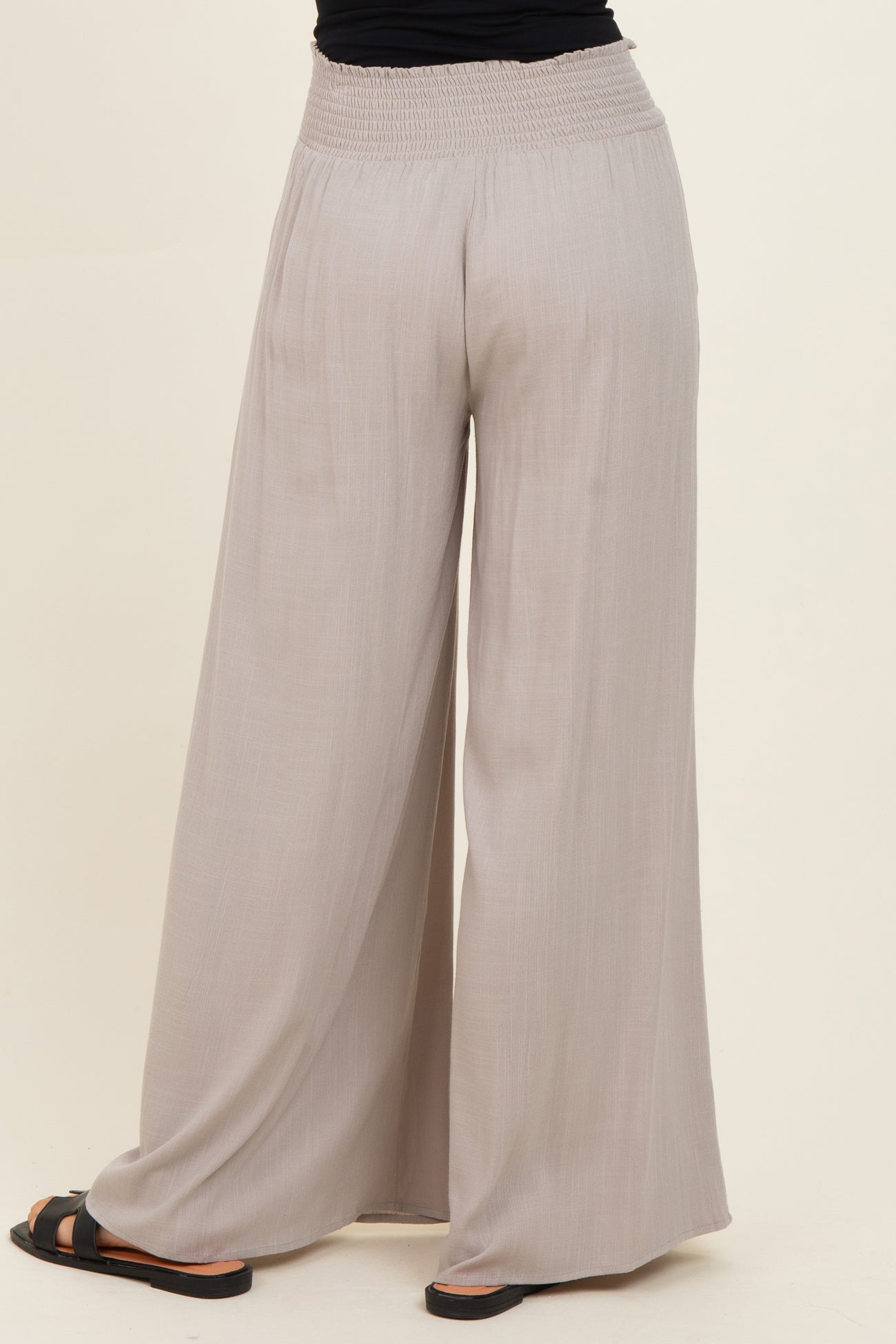 woman wearing light gray wide-leg pants with a smocked waistband and black sandals