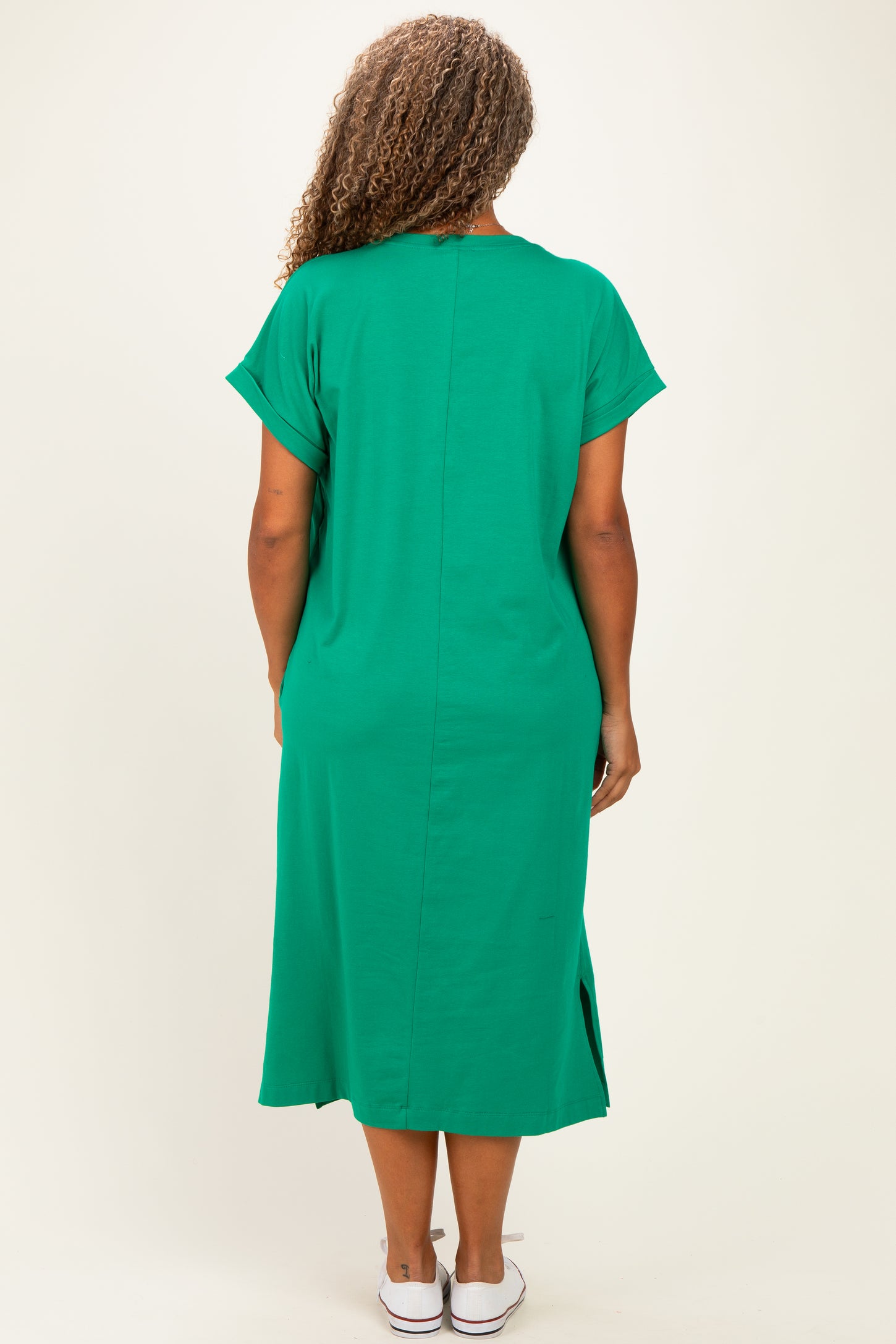 woman wearing a green short sleeve plus size dress with side slits and a relaxed fit, viewed from the back