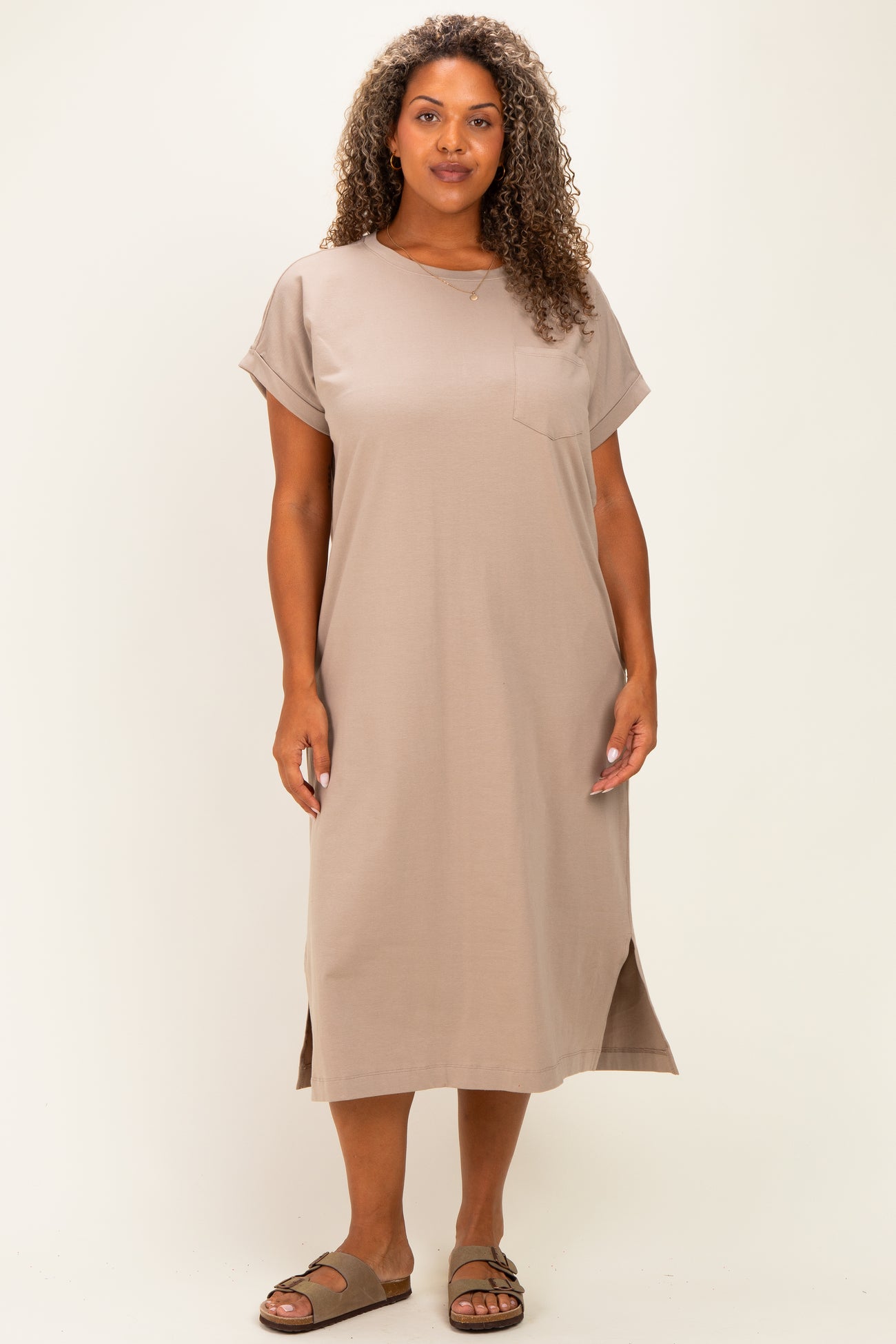woman wearing a taupe short sleeve midi dress with a pocket and side slits, standing on a plain background