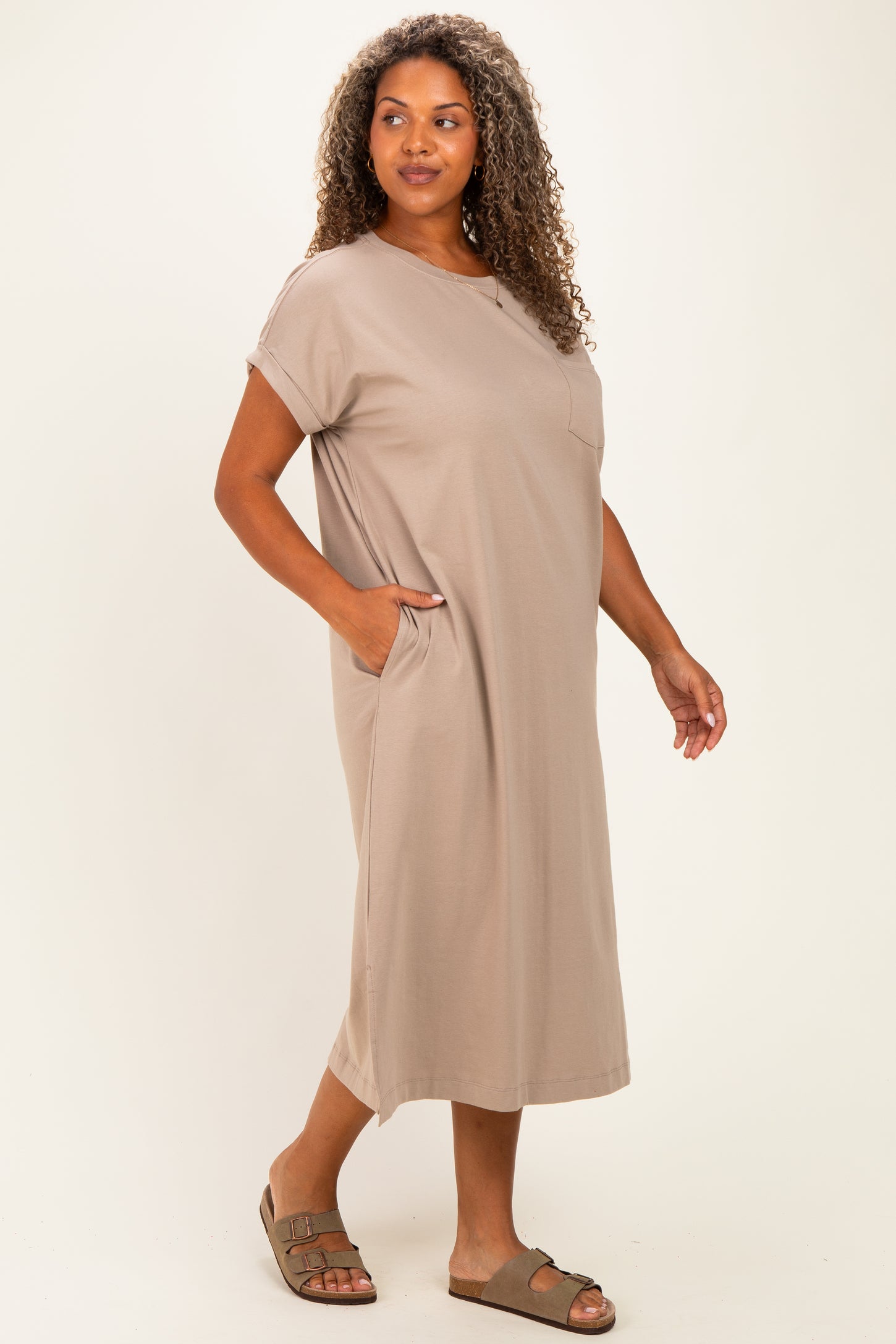 woman wearing a taupe plus-size midi dress with short sleeves and pockets, styled casually with brown sandals