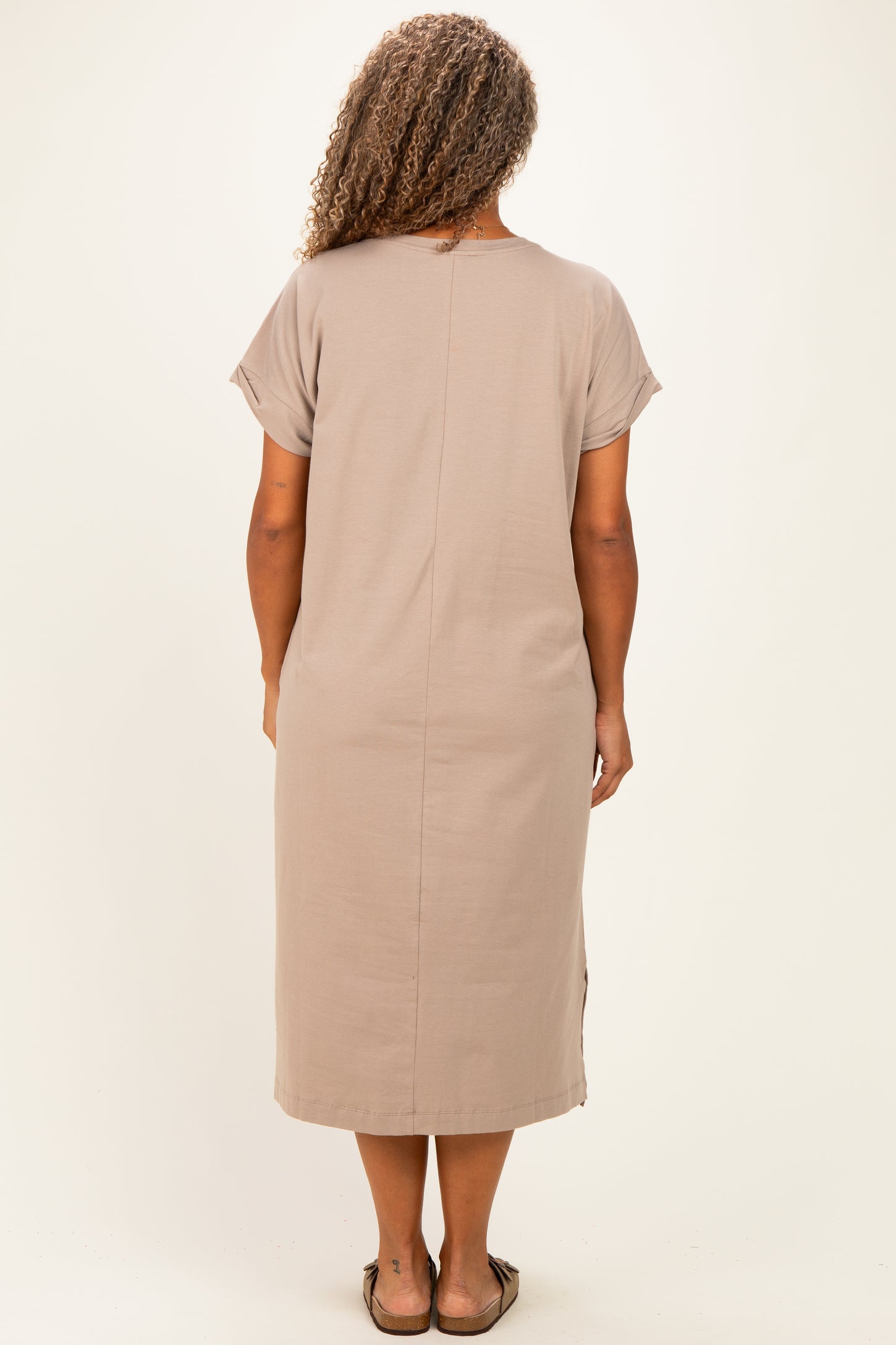 woman wearing a taupe short sleeve plus-size dress with a straight cut and side slits, viewed from the back