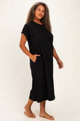 woman wearing a black plus size midi dress with short sleeves and side pockets, standing casually