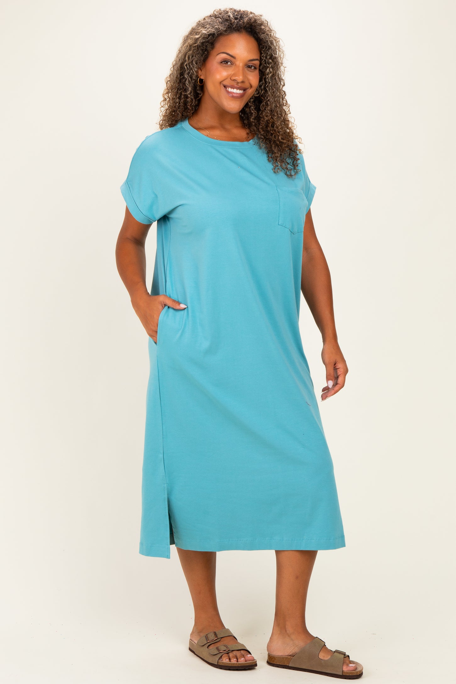 woman wearing a teal plus-size midi dress with short sleeves and side pockets, standing with a smile