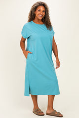 woman wearing a teal plus-size midi dress with short sleeves and side pockets, standing with a smile