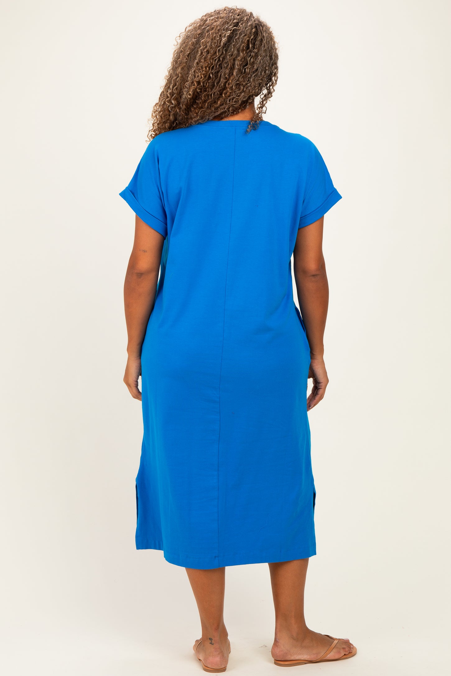woman wearing a bright blue plus size midi dress with short sleeves and side slits, seen from the back