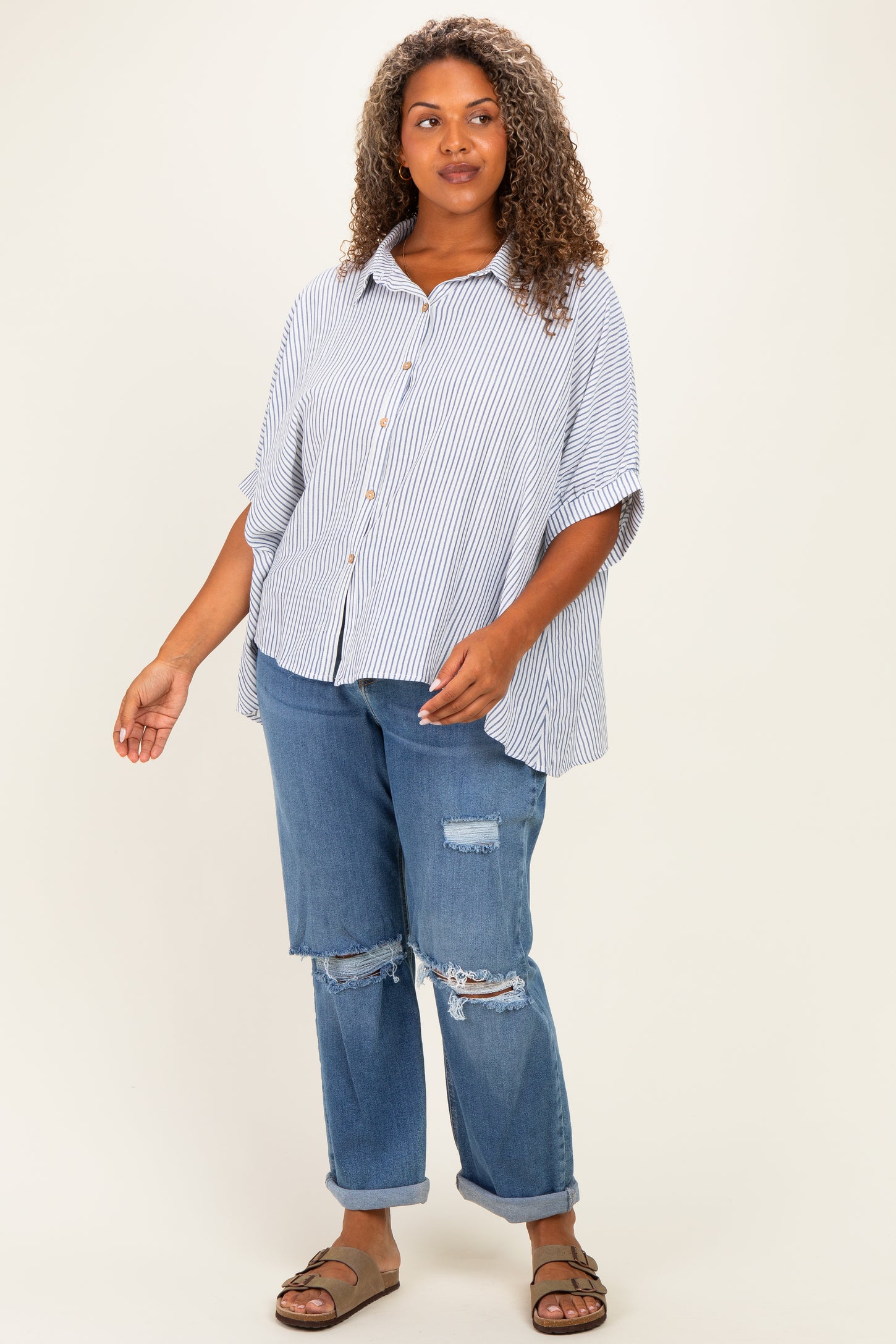 woman wearing a striped button-up poncho top with oversized sleeves and distressed denim jeans
