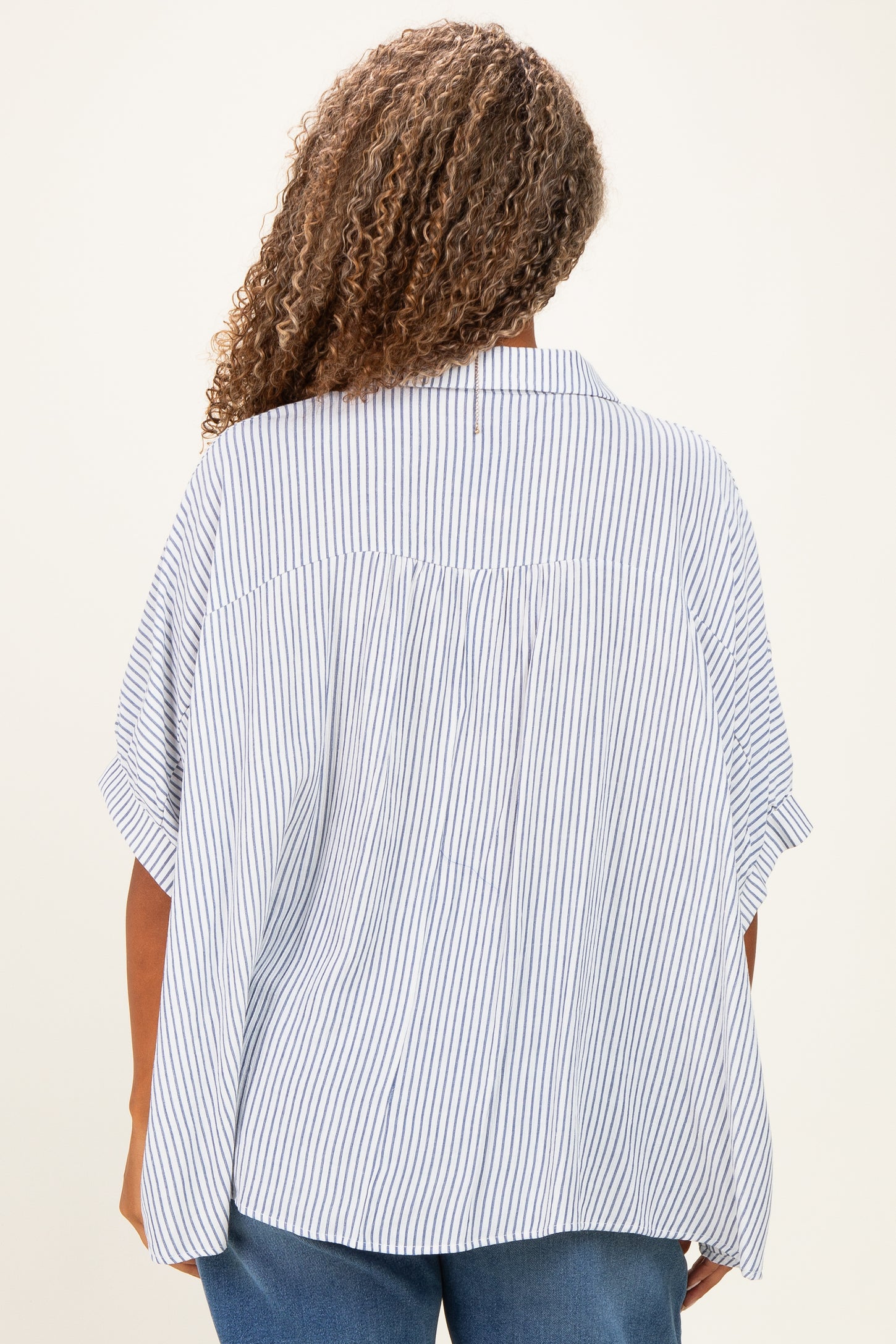 woman wearing a loose-fitting blue and white striped plus size blouse, view from the back