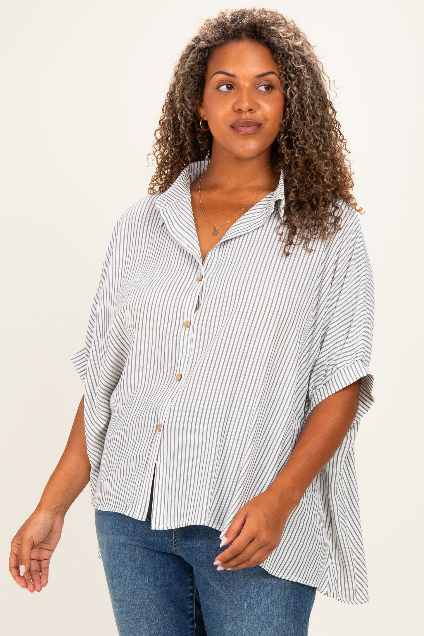 woman wearing a striped button-up blouse with a relaxed fit and rolled sleeves, paired with blue jeans