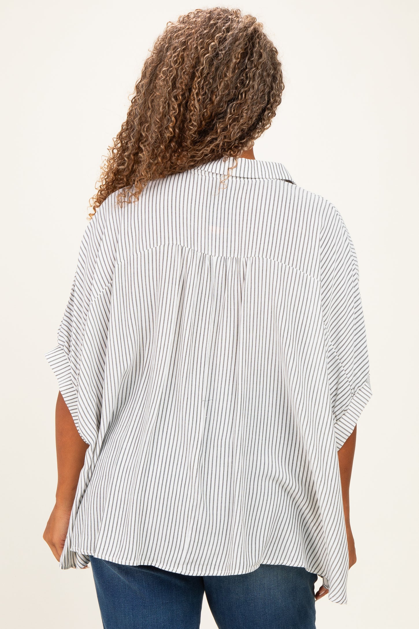 woman wearing a loose-fitting striped plus-size top with wide sleeves and a back pleat detail.