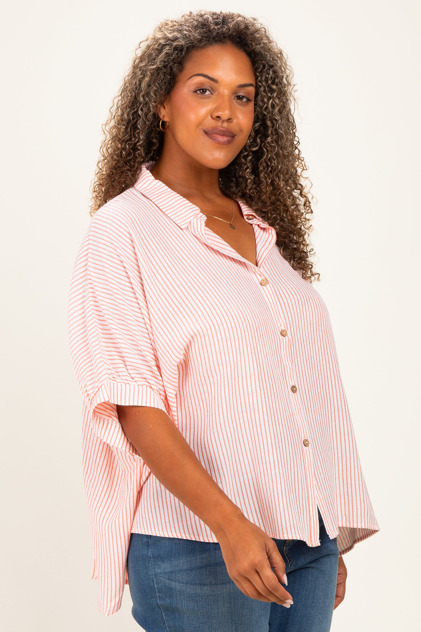 woman wearing a pink and white striped plus size button-up shirt with rolled sleeves and a relaxed fit