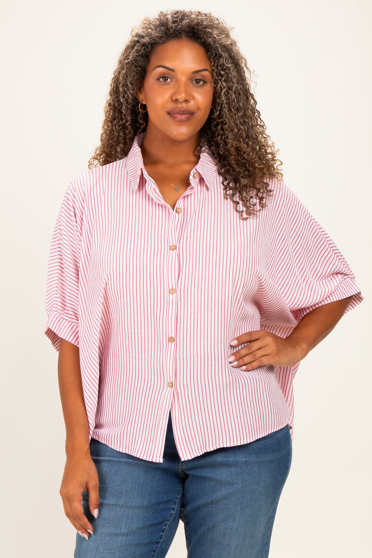 woman wearing a pink and white striped plus size button-up shirt with short sleeves and a relaxed fit, paired with blue jeans