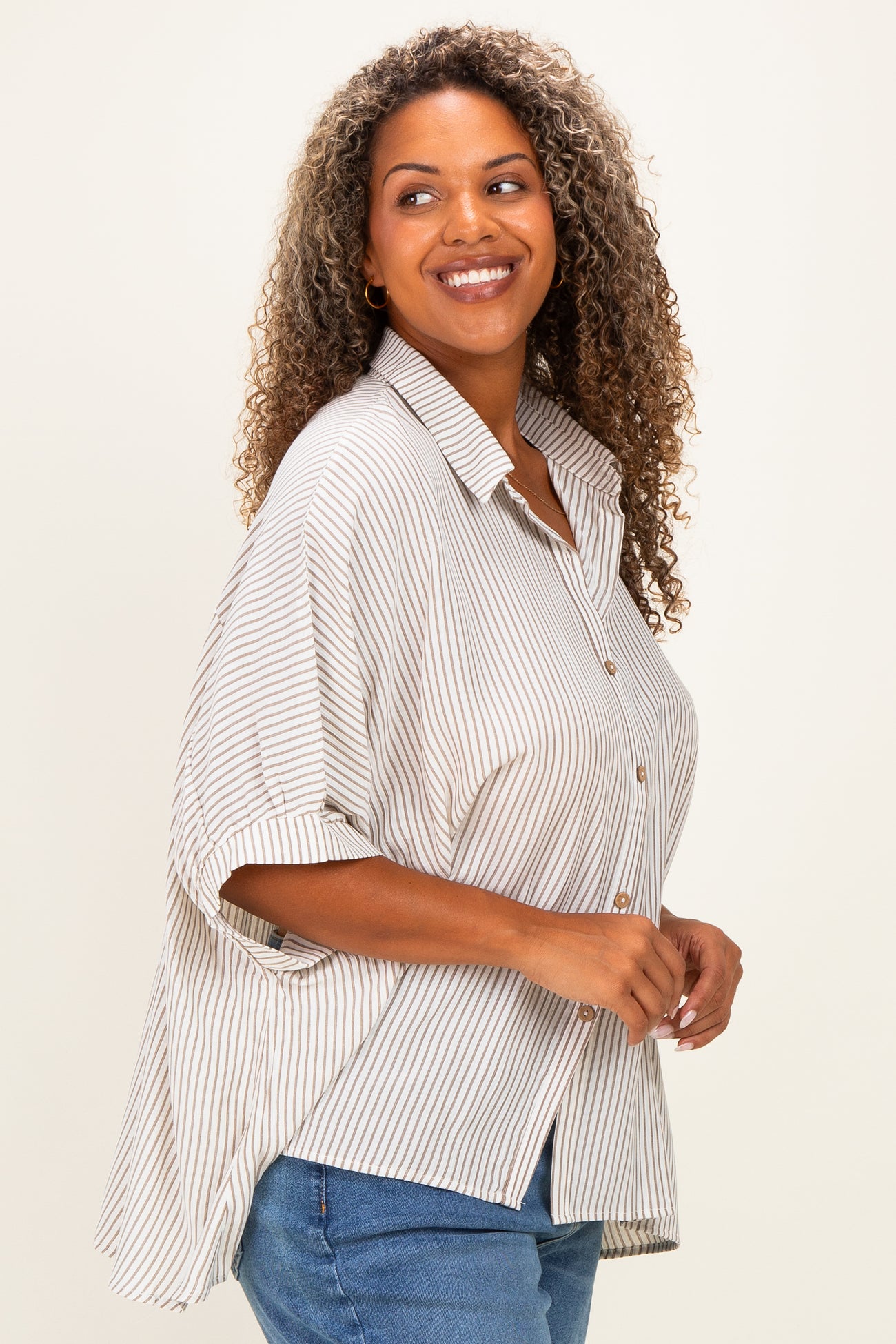 woman wearing a beige and white striped oversized button-up shirt with rolled sleeves and blue jeans