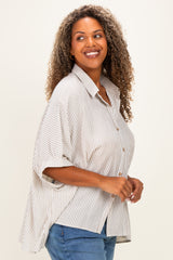 woman wearing a beige and white striped oversized button-up shirt with rolled sleeves and blue jeans