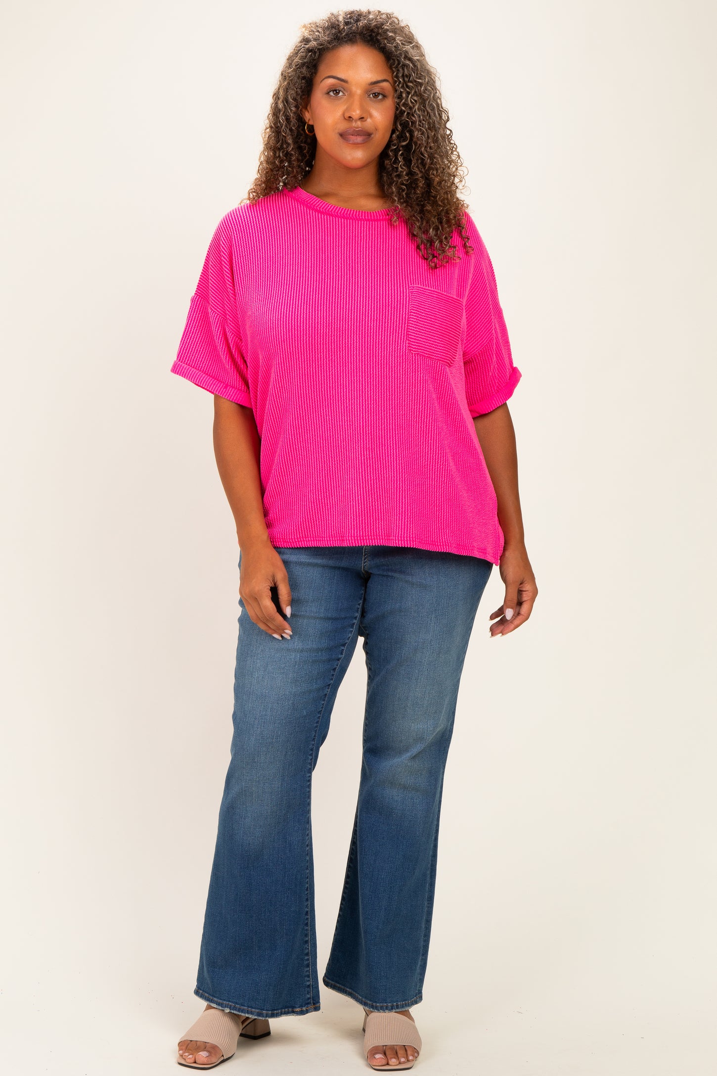 woman wearing a bright pink oversized ribbed t-shirt with short sleeves and a pocket, paired with flared jeans