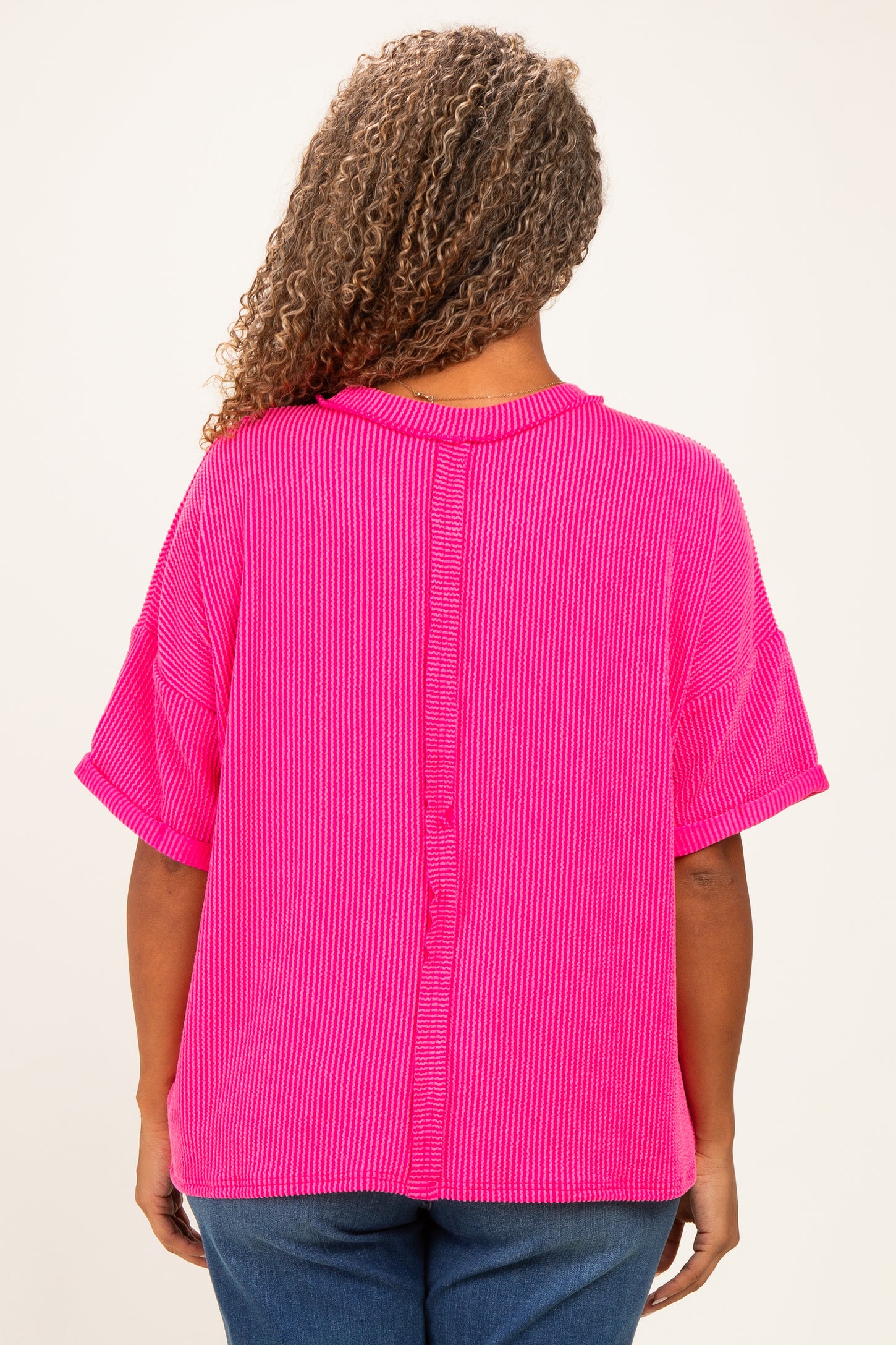 woman wearing a bright pink short sleeve plus size top with a button detail down the back