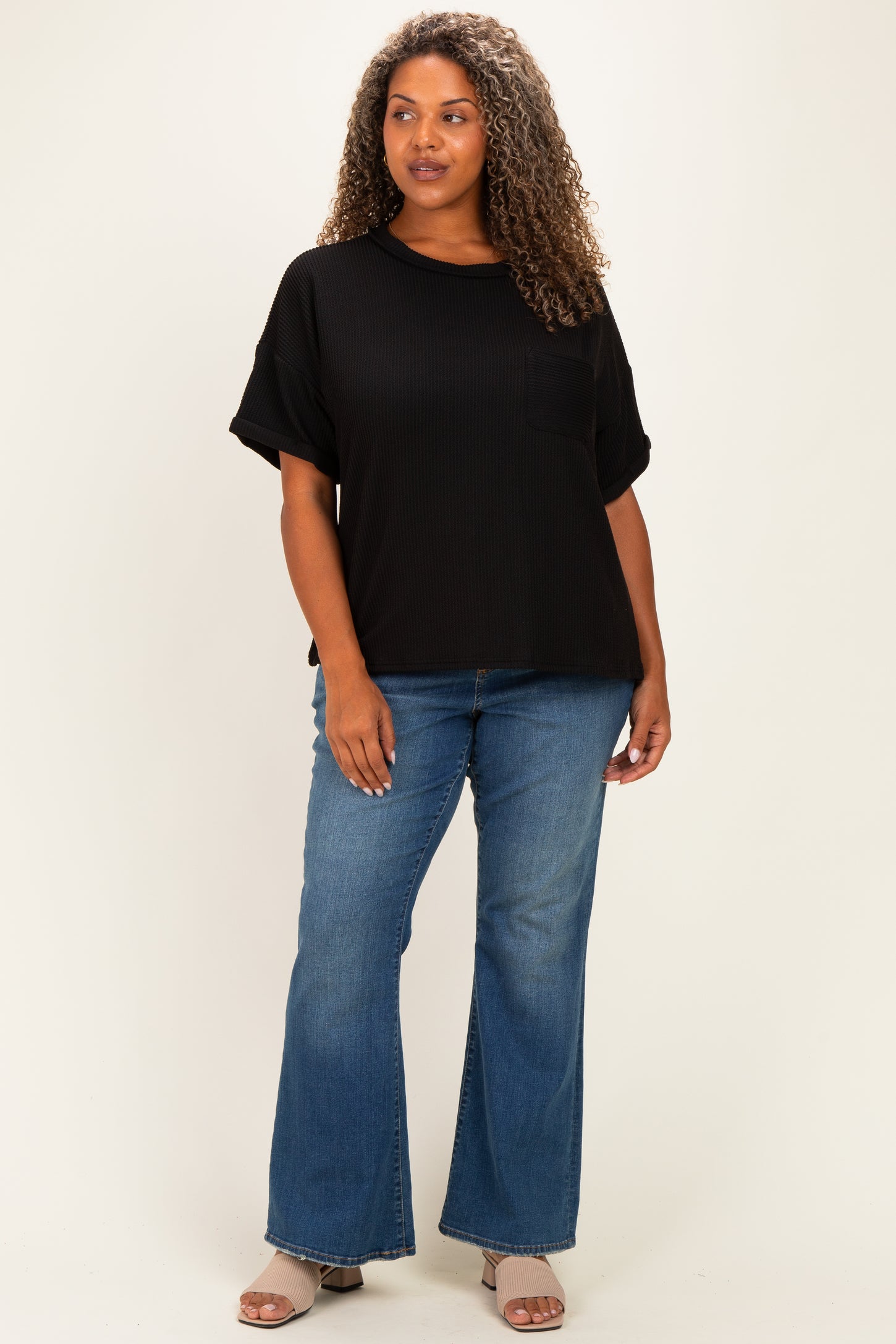 woman wearing a black oversized ribbed top with a pocket and flared blue jeans