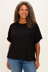 woman wearing a black ribbed plus size top with short sleeves and a front pocket, smiling against a neutral background