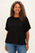 woman wearing a black ribbed plus size top with short sleeves and a front pocket, smiling against a neutral background