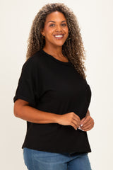 woman wearing a black ribbed short sleeve top and blue jeans, smiling while standing against a light background