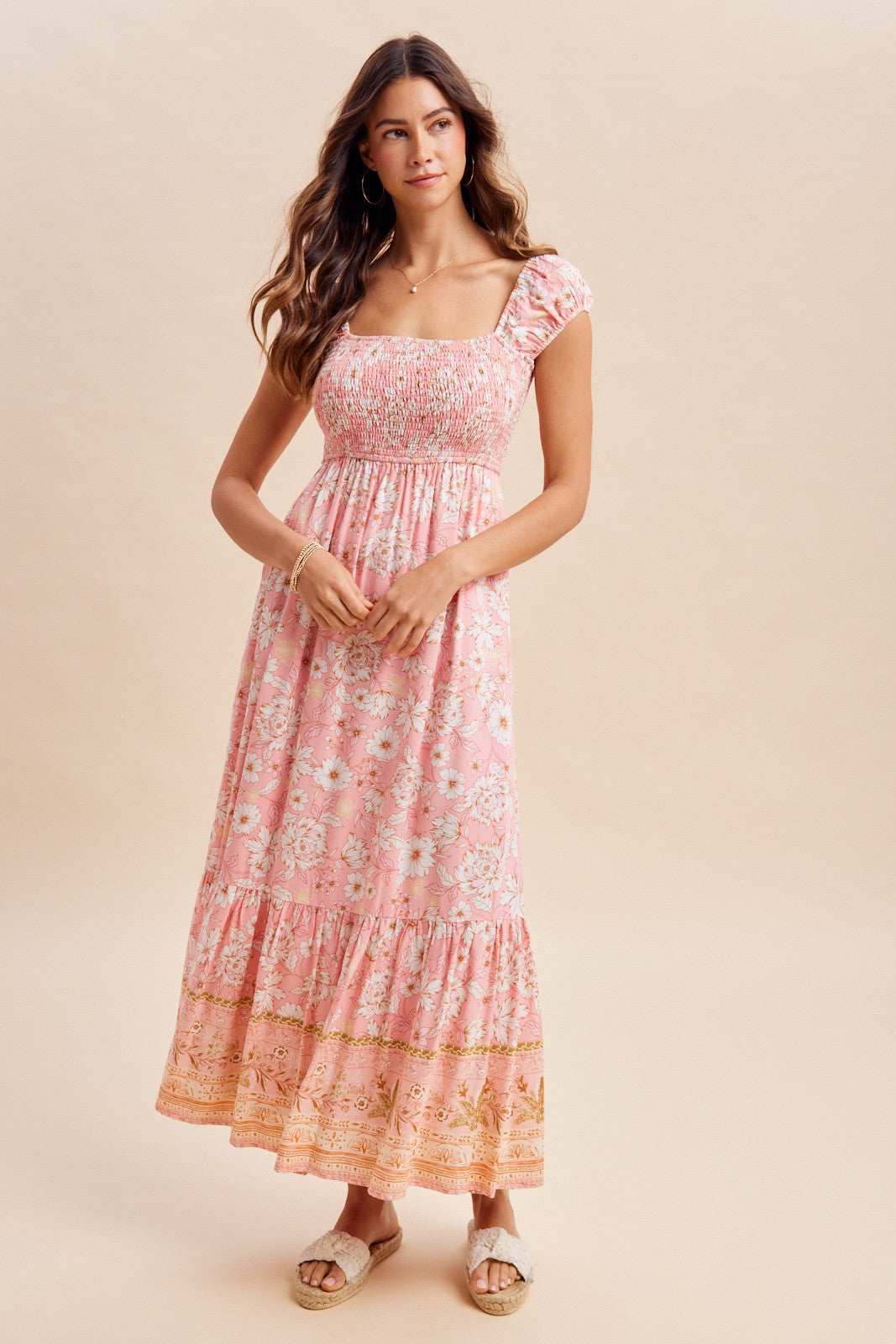 woman wearing a pink floral maxi dress with smocked bodice and ruffled sleeves, standing against a light background