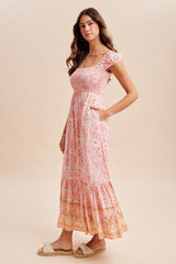 woman wearing a pink floral maxi dress with a square neckline and puff sleeves, featuring a tiered hem and pockets