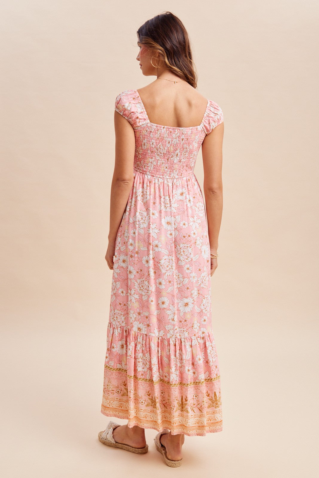woman wearing a pink floral maxi dress with a square neckline and smocked bodice, showing a tiered skirt from the back