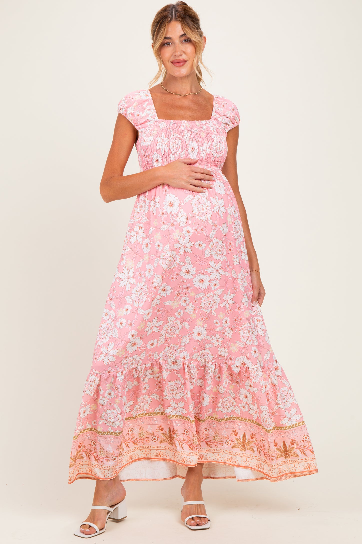 woman wearing a pink floral maxi maternity dress with a square neckline and ruffled hem, holding her baby bump
