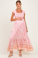 woman wearing a pink floral maxi maternity dress with a square neckline and ruffled hem, holding her baby bump