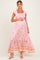 woman wearing a pink floral maxi maternity dress with a square neckline and ruffled hem, holding her baby bump