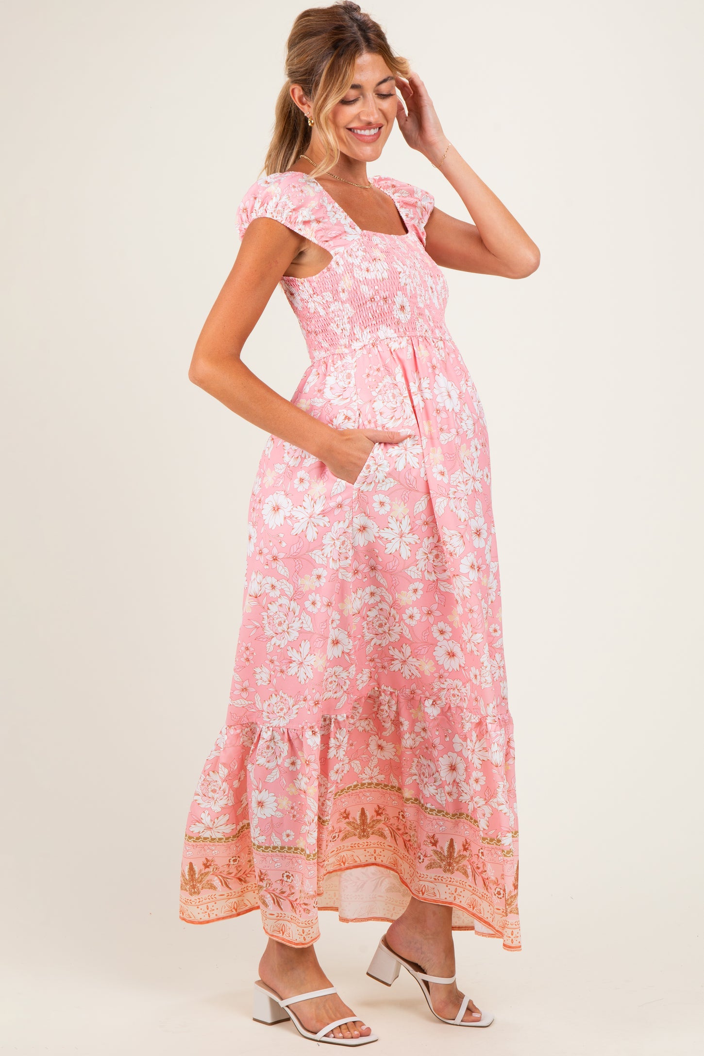 woman wearing a pink floral maxi maternity dress with cap sleeves and pockets, showing her baby bump