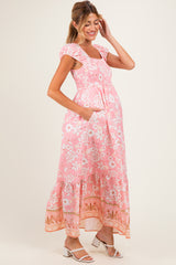woman wearing a pink floral maxi maternity dress with cap sleeves and pockets, showing her baby bump
