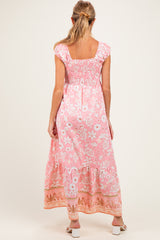 woman wearing a pink floral maternity maxi dress with ruffled sleeves and smocked bodice, displaying her baby bump
