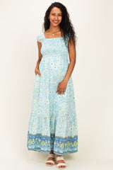 woman wearing a light blue floral maternity maxi dress with smocked bodice and pockets, showcasing her baby bump