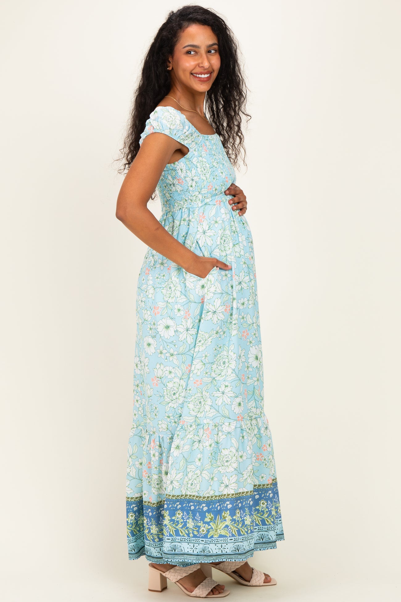 woman wearing a blue floral maternity maxi dress with short sleeves and pockets, highlighting her baby bump