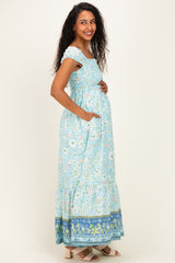 woman wearing a blue floral maternity maxi dress with short sleeves and pockets, highlighting her baby bump