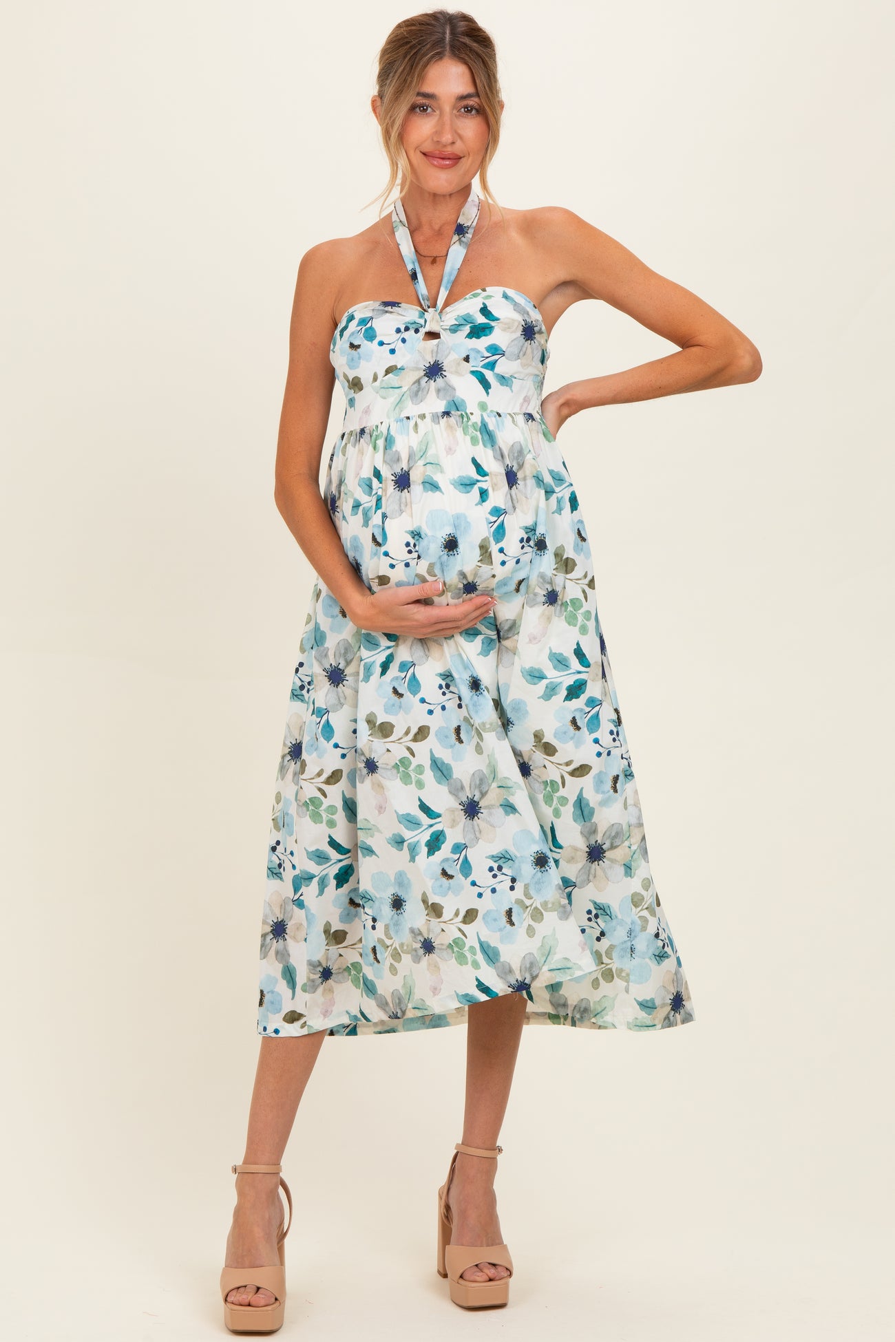 woman wearing a floral strapless maternity dress, showing her baby bump while posing against a light background
