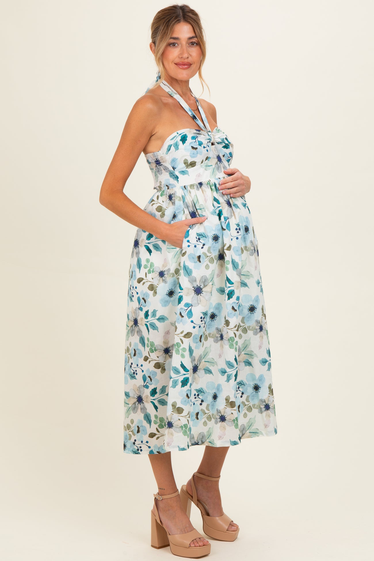 woman wearing a floral print maternity dress with a halter neck and pockets, showing a baby bump