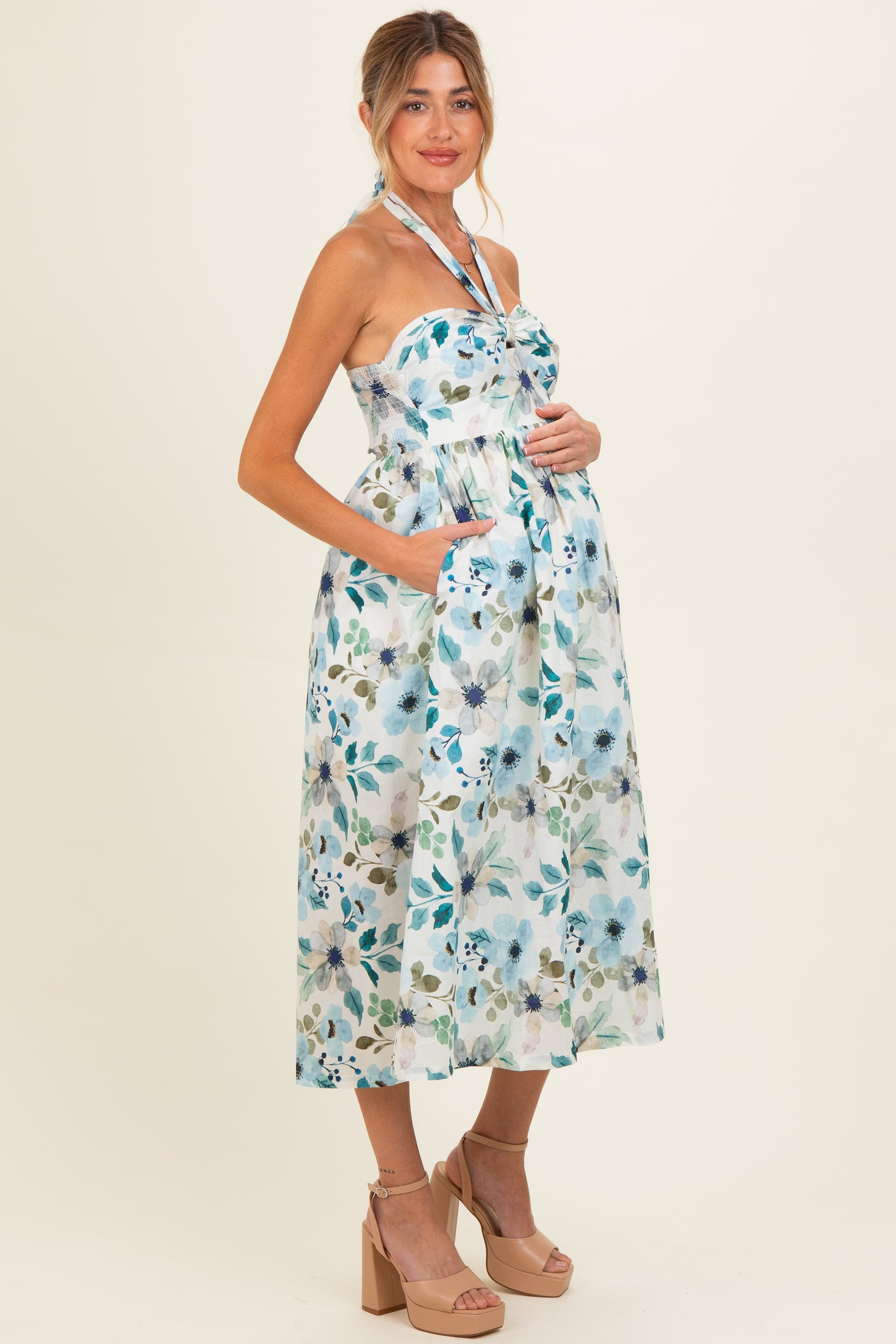 woman wearing a floral print maternity dress with a halter neck and pockets, showing a baby bump