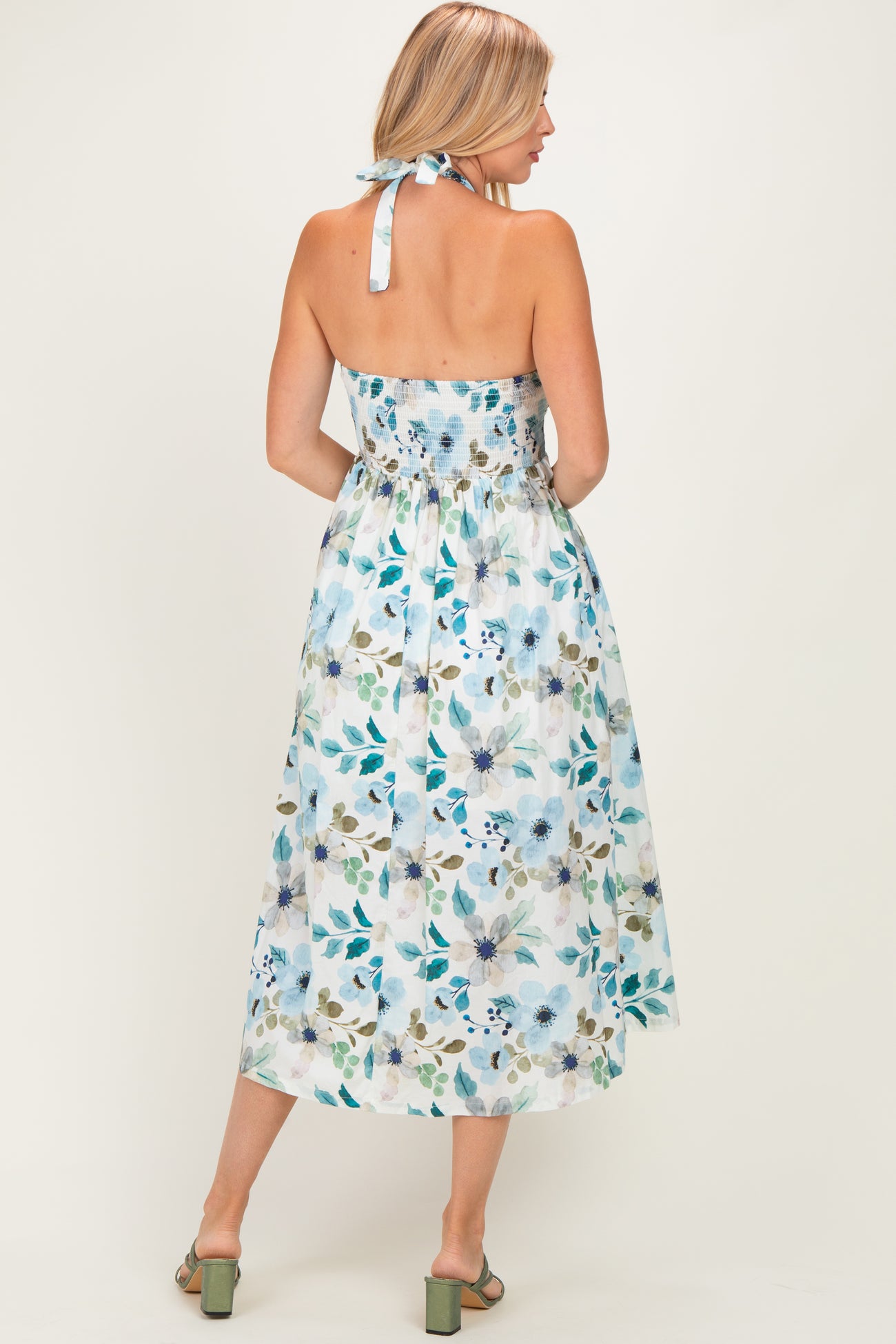 woman wearing a floral print midi dress in light blue with a smocked back and halter neck, showing the back view