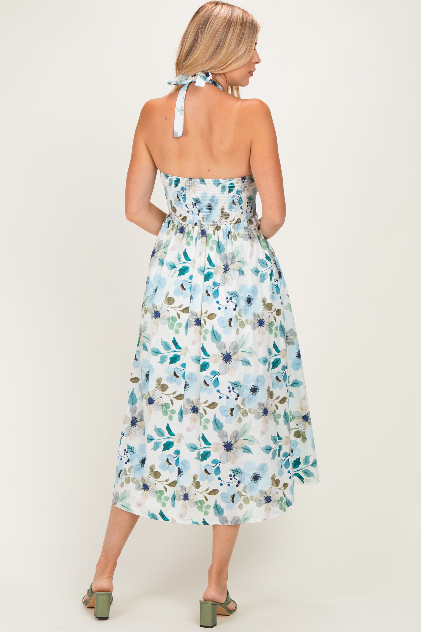 woman wearing a floral print midi dress in light blue with a smocked back and halter neck, showing the back view