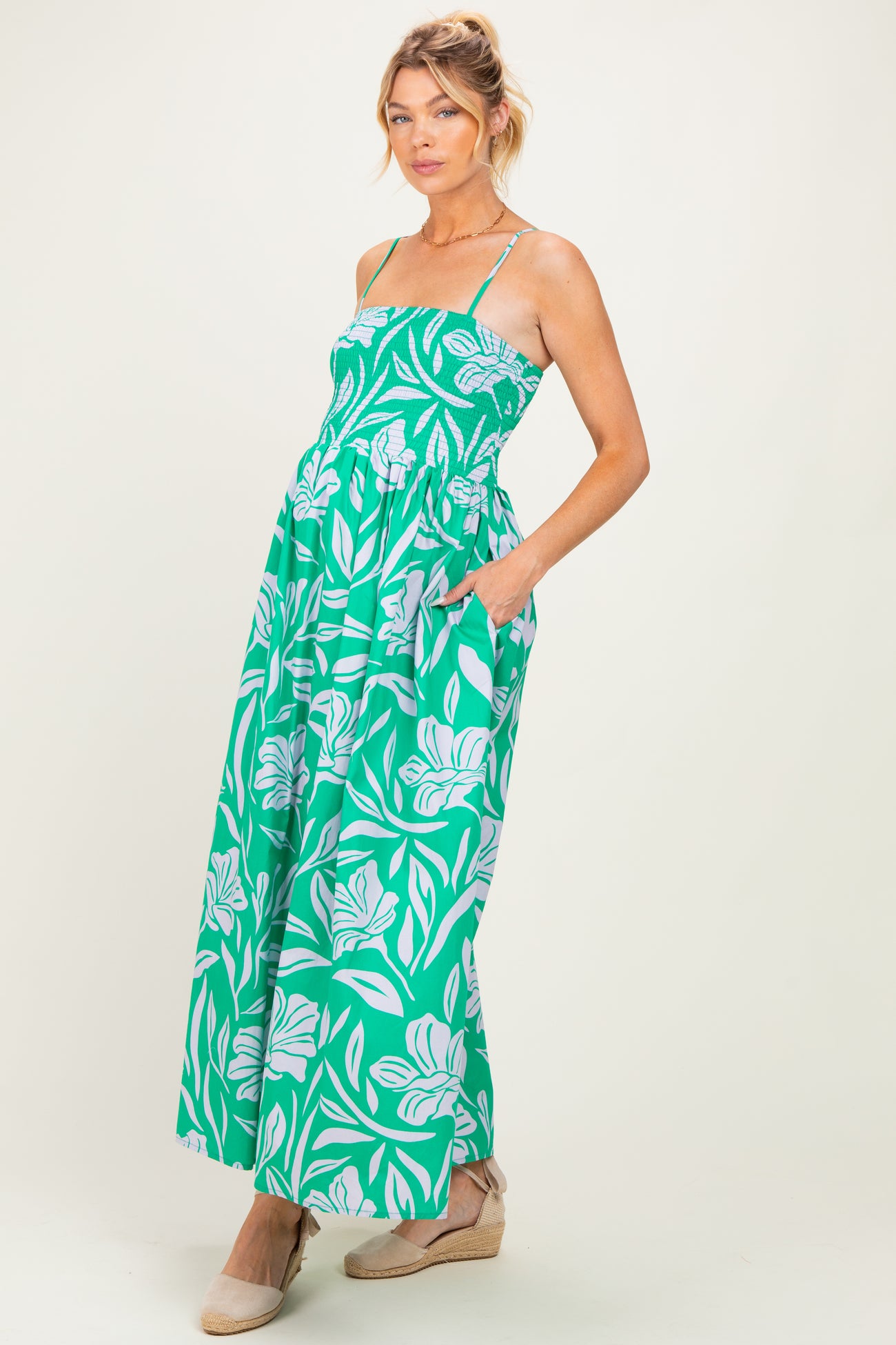 woman wearing a green floral maternity maxi dress with a smocked bodice and pockets, holding her baby bump