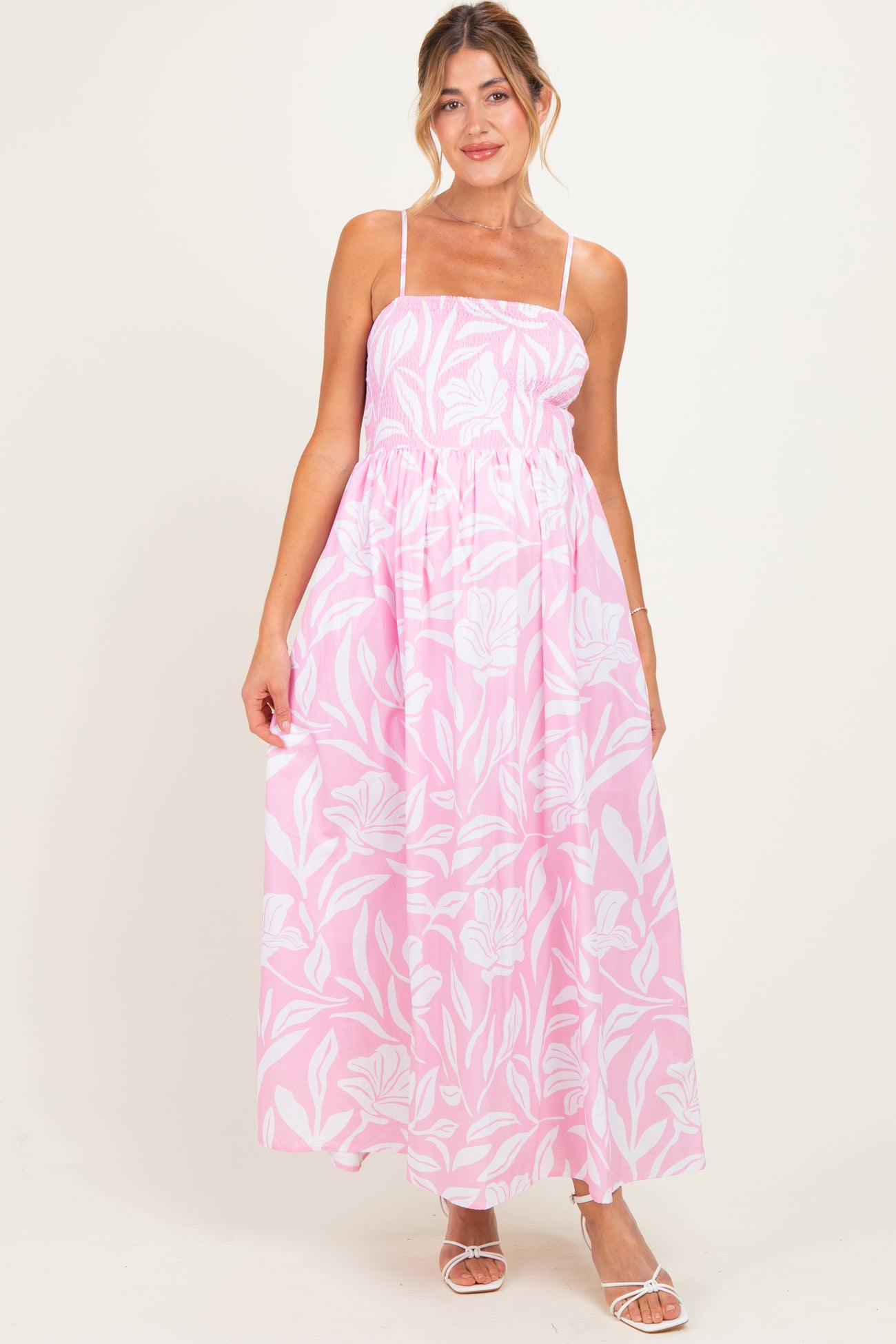 woman wearing a pink floral maternity maxi dress with spaghetti straps and a smocked bodice, showcasing a baby bump