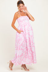 woman wearing a pink floral maternity maxi dress with spaghetti straps and pockets, showcasing her baby bump