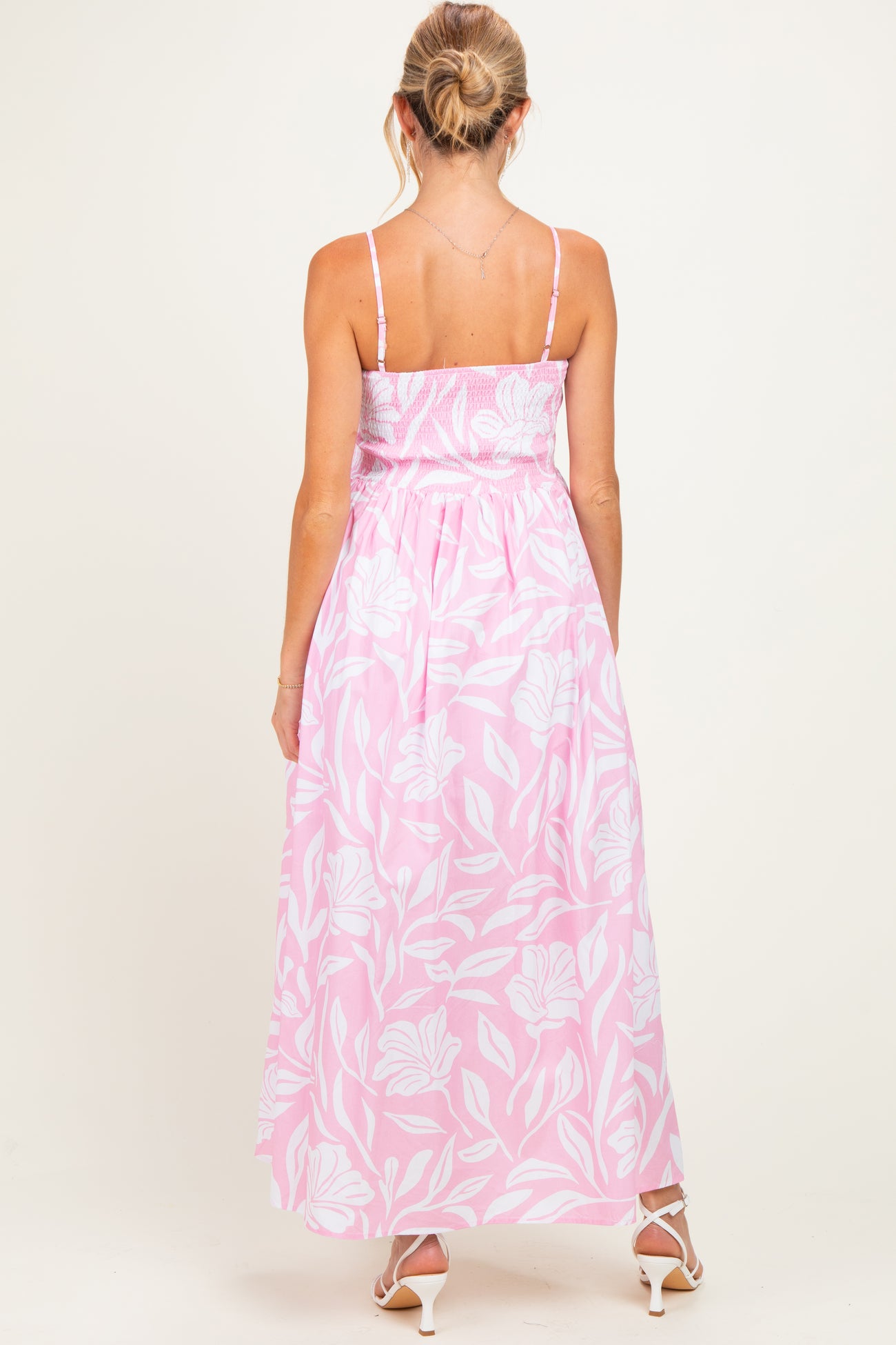woman wearing a pink floral maternity maxi dress with a smocked bodice and adjustable straps, showing the back view