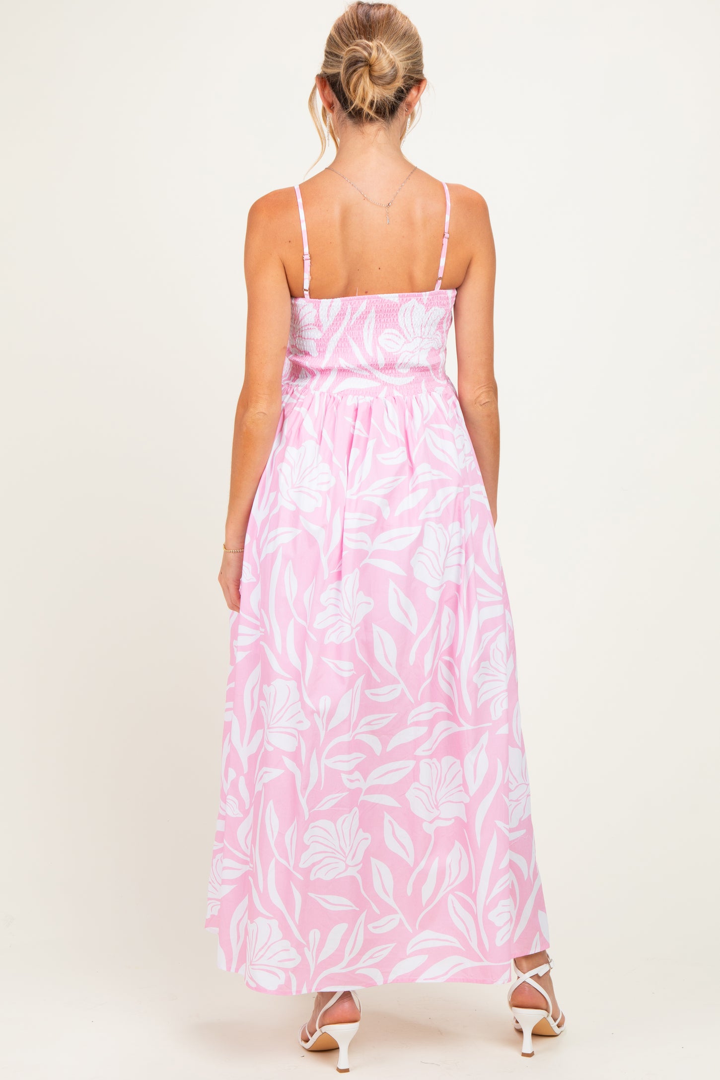 woman wearing a pink floral maternity maxi dress with a smocked bodice and adjustable straps, showing the back view
