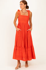 woman wearing a bright red maxi dress with decorative ties, eyelet details, and pockets